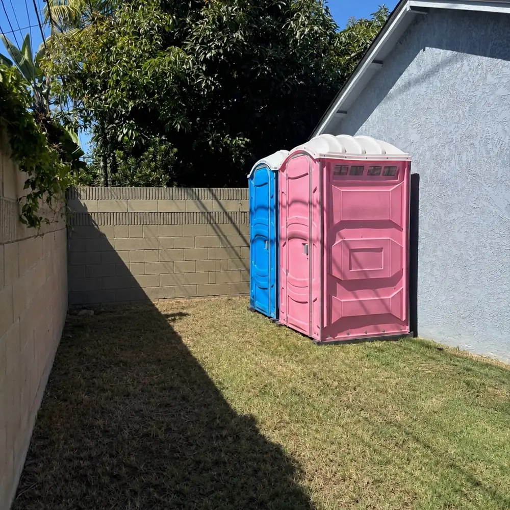 Two porta potties placed along a backyard fence