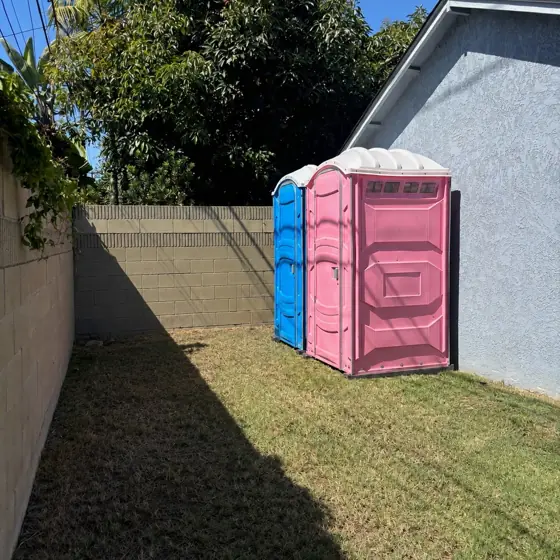 Two porta potties along a backyard fence for a party