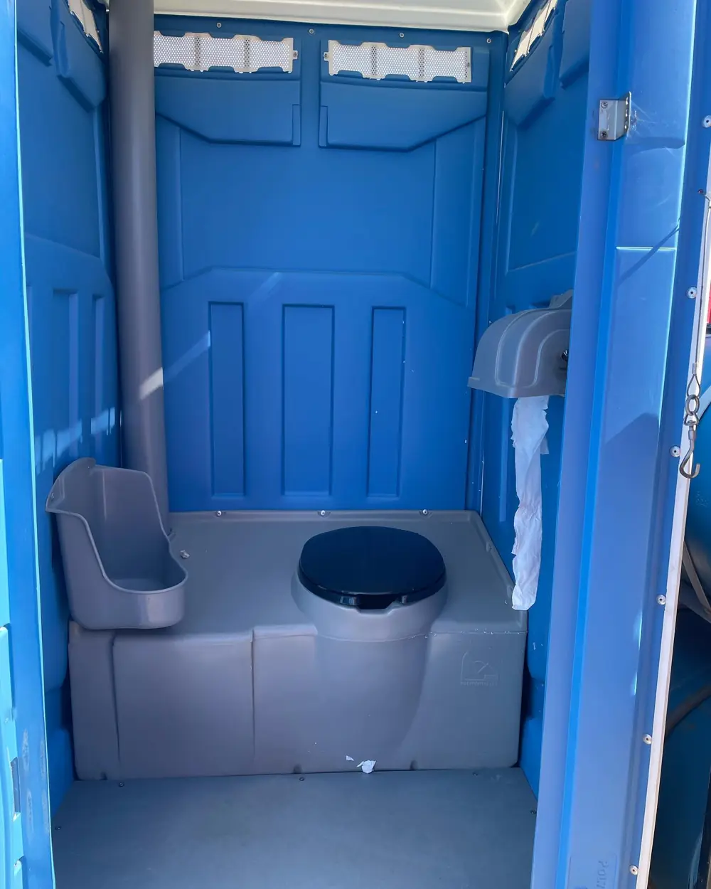 Inside a standard porta potty showing the seat, urinal and paper holder
